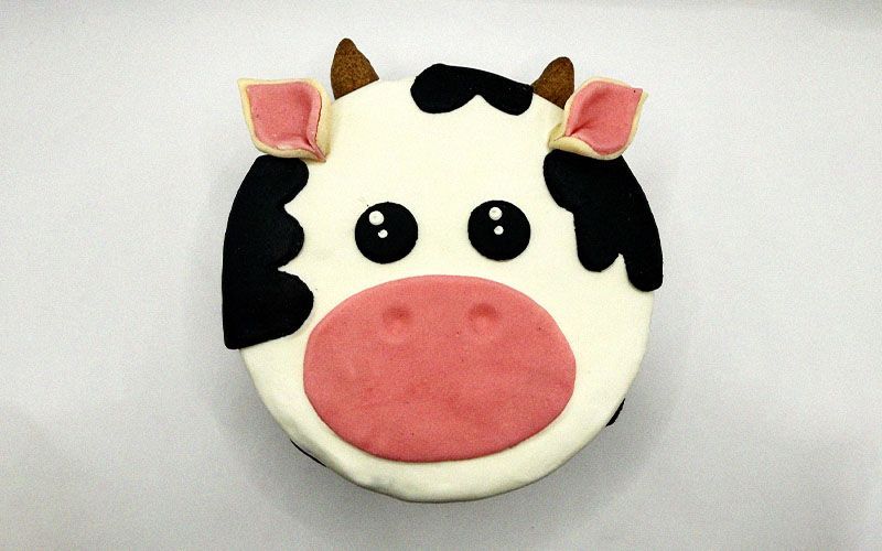 cake designed to resemble a cow featuring black and white icing and decorative details like ears and a tail